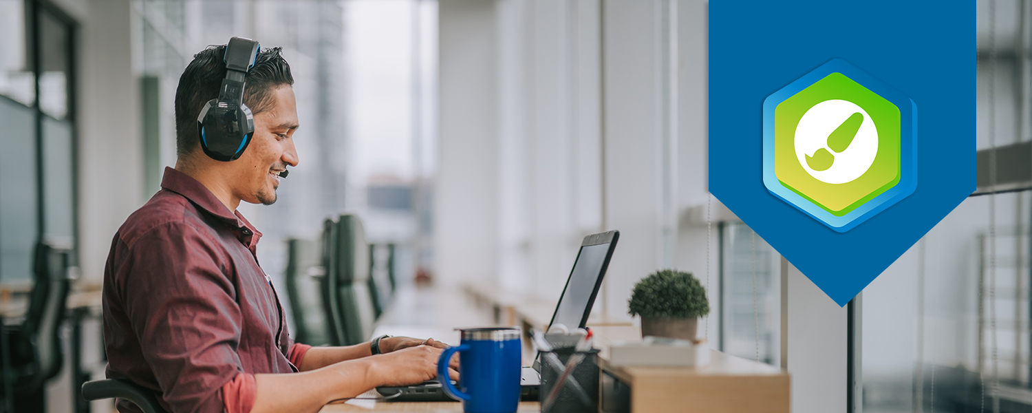 Man looking at laptop in an office setting. The DesignPLUS logo is displayed on the right side of the photo.