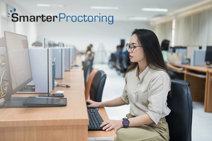 Woman taking an exam on a computer in a testing facility, SmarterProctoring logo in upper left corner