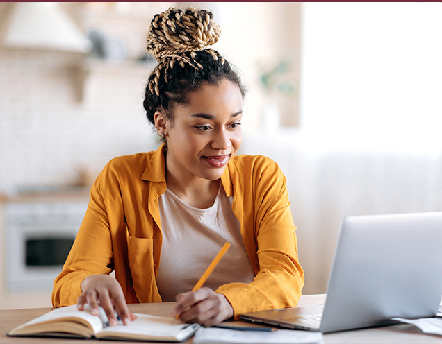 Photo of woman working on a laptop and writing notes