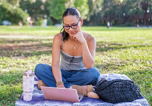 Photo of a student sitting on the campus lawn working on her laptop