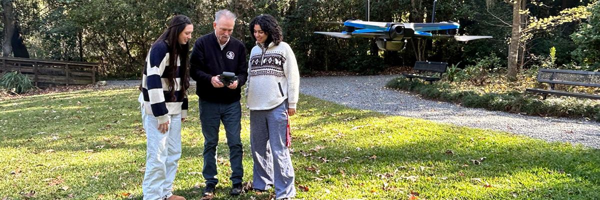 Two interns and supervisor fly drone in an outdoor setting