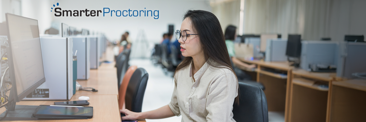 Woman taking an exam on a computer in a testing facility, SmarterProctoring logo in upper left corner