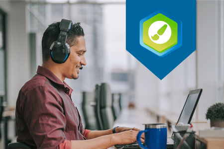 Man looking at laptop in an office setting. The DesignPLUS logo is displayed on the right side of the photo.