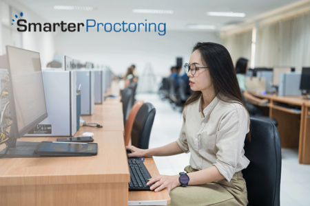 Woman taking an exam on a computer in a testing facility, SmarterProctoring logo in upper left corner