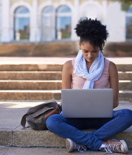 Female student sitting on campus steps working on a computer