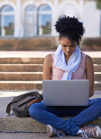 Female student sitting on campus steps working on a computer