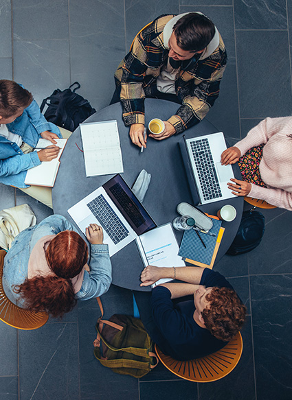 Five people sitting around a table working on computers and talking